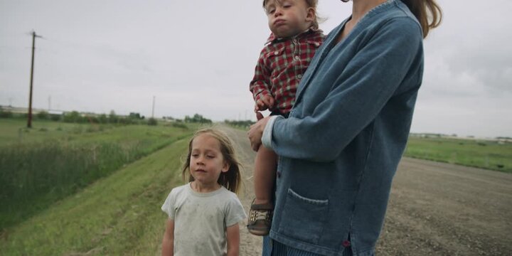 Mother holding her toddler on a country road with another child nearby