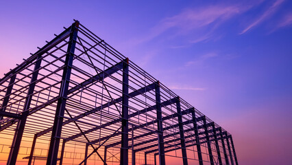 Fototapeta premium Silhouette metal structure of industry warehouse factory building with steel framework in construction site against colorful evening sky background, low angle view with copy space