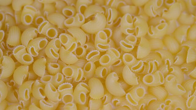 Pasta shells display. Uncooked macaroni in closeup shot. Densely packed dry pasta with textured edges. Goldenhued dry pasta shells captured with soft studio illumination