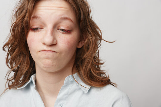 Young woman with wavy hair looks down with a doubtful expression wearing a light shirt. Concept of uncertainty, hesitation, and contemplation on neutral background.