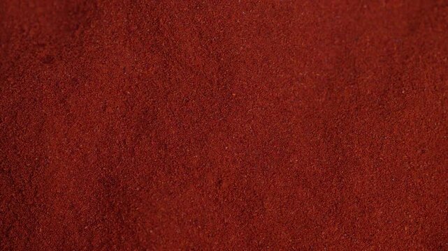 Closeup red paprika powder texture, rich fine granules spread across surface, deep warm tones, earthy spice detail ideal for food packaging and seasoning visuals