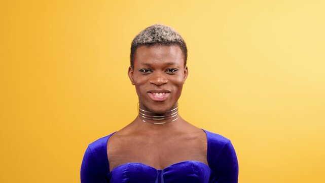 Confident androgynous black person in a blue velvet top looking up and smiling. Non binary individual expressing pride and happiness