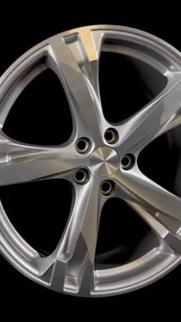 A close-up shot of a sleek, modern silver alloy wheel on a black background, showcasing its design and details