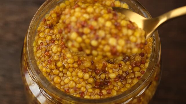 French wholegrain dijon mustard scoop with spoon from jar, close up 