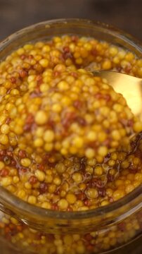 Wholegrain dijon mustard scoop with spoon from jar, close up 