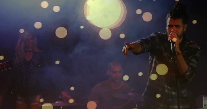 Lead singer entering right, moving center, singing into mic while bokeh lights engaging music crowd