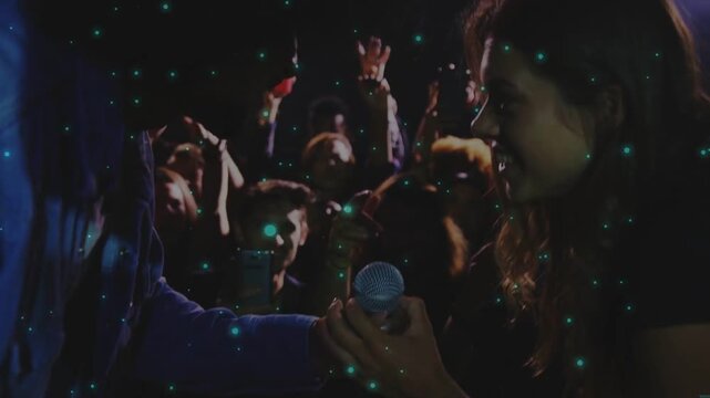 Man offering round prop to woman at music venue to engage crowd, teal particles overlaying frame