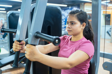 Fototapeta premium Indian Woman Performing Butterfly Exercise on Pec Deck Machine During Chest Workout in Modern Gym