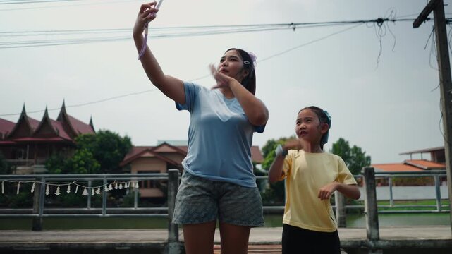 A young Asian girl with a girl doing a dance for tik tok holding the smartphone with one hand