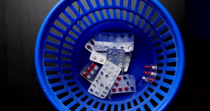 Close up of used pill blisters being thrown into a blue waste bin to symbolize medical malpractice and pharmacy negligence issues.