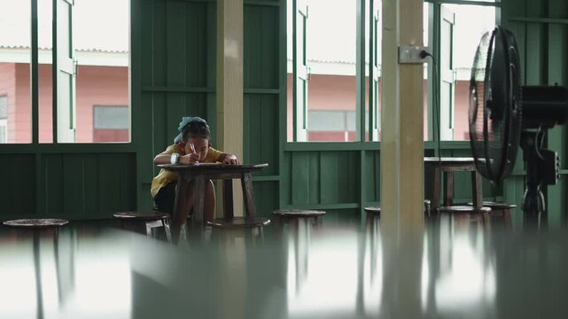 A little girl studies alone in an open quiet classroom with green walls concentrating on writing at her desk