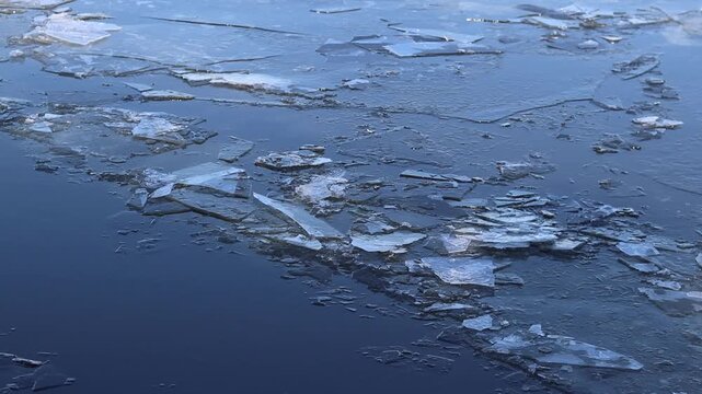 Cracked melted ice moves along the surface of the river. The ice is partially broken, due to which the layering of transparent ice plates is visible on the surface. Melting ice in the river. Winter