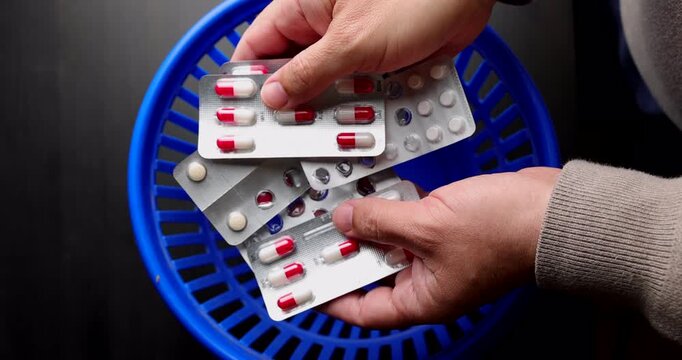 Discarding empty and half used pill blisters in a blue waste basket for illustrating medicine malpractice and poor health habits.
