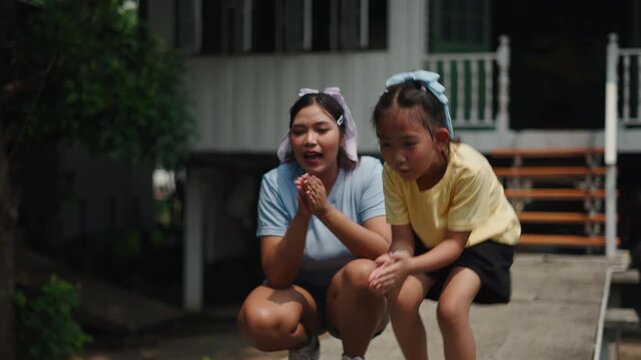 Asian woman and girl with bows on their heads crouch next to each other smiling and each play with a dog