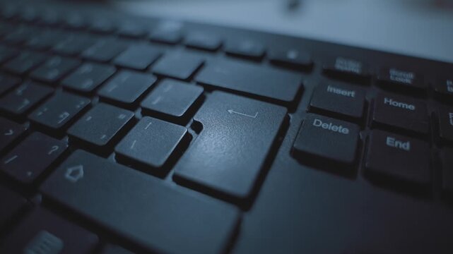 Extreme close up on finger pressing on enter or return key on computer keyboard. Person clicking on button to confirm or execute command or submit data. Dark room or office desk. Hacker or programmer