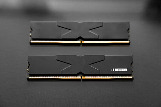 Black DDR5 RAM memory modules placed on a dark, glossy surface. RAM shortages on the market, rising prices, and increased demand driven by the growing need for AI training.