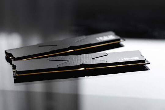 Black DDR5 RAM memory modules placed on a dark, glossy surface. RAM shortages on the market, rising prices, and increased demand driven by the growing need for AI training.