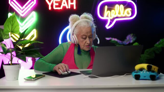 Contemporary elderly woman in headset playing multiplayer game on laptop
