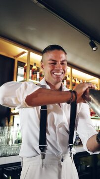 Professional bartender smiling and shaking a stainless steel shaker. Young mixologist making a drink behind the bar in a stylish establishment