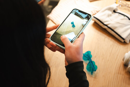 A person holds a smartphone, capturing a photo of small blue objects and clothing laid out on a wooden surface.
