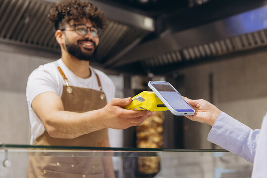 Arab man smiling while accepting contactless payment from a customer using a smartphone at a food stall