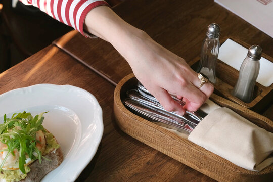 Woman hand taking cutlery from wooden holder on restaurant table. Dining experience, table etiquette and food lifestyle concept with plated meal