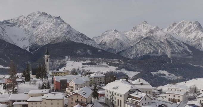 Cinematic aerial view of a Swiss Alpine village in Engadin valley, with snow covered rooftops and dramatic peaks creating a serene winter landscape for luxury travel, upscale tourism and premium stays