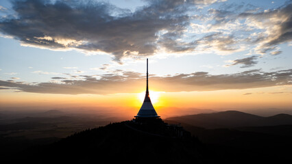 At dusk, Jested Mountain Hotel stands beautifully against a vibrant sky over Liberec. The modern architecture is highlighted as the sun sets, casting warm hues across the landscape. © pyty