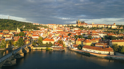 Obraz premium The early morning light casts a warm glow over the historic Charles Bridge and the majestic Prague Castle. The Vltava River reflects the stunning architecture of the city, creating a beautiful scene.