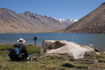 Fototapeta premium Amazing scenery of turquoise Guharrez (Zaroshkul) Lake and silhouette of sitting trekker in Pamir Mountains,Tajik National Park, Gorno - Badakhshan, Tajikistan