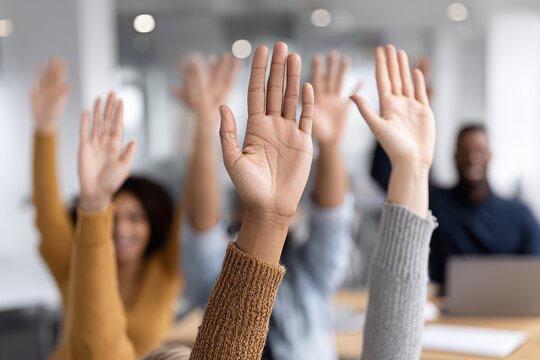 A group of diverse business people raising their hands during a meeting or conference, showing participation, agreement, or volunteering in a bright office setting.