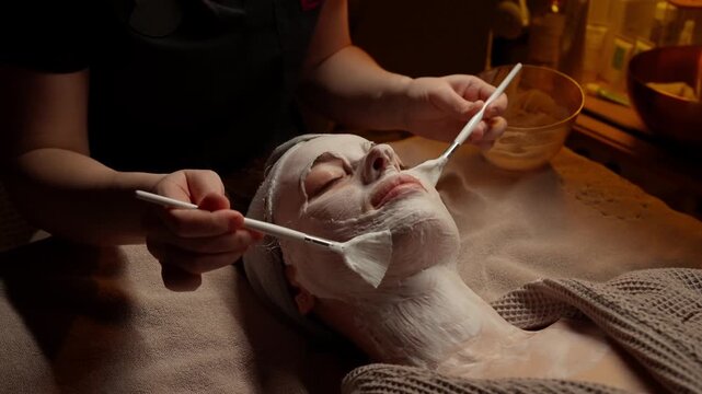 Relaxing spa facial treatment with soothing white mask application on woman face and neck during professional skincare session in warm ambient lighting