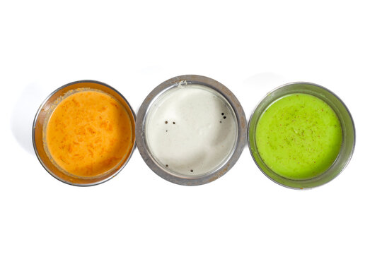 South indian trio of red, coconut, and green chutneys served in stainless steel bowls on white background