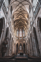 Obraz premium Visitors explore the gothic interior of St. Vitus Cathedral at Prague Castle. Tall arches and stained glass windows create a historic atmosphere in this famous location.