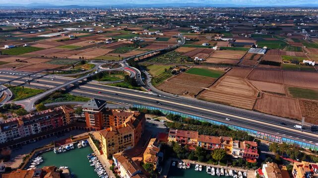 Beautiful houses with sea-green waterscape and boats around. Port Saplaya, Valencia, Spain. Huge road system in the backdrop. Aerial view.