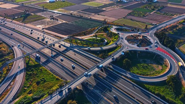 Setting sun lights the multi-lane highway with trestles and roundabout. Agricultural fields in the backdrop.