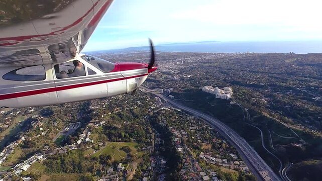 Closeup profile view of a small Cessna airplane flying above the western Santa Monica Mountains and Sepulveda Pass sections of Los Angeles, California on a late afternoon.
