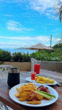 Tropical breakfast served on outdoor terrace overlooking the ocean. Plate with scrambled eggs, potatoes, fried plantains and pineapple on a wooden table with sea view in Costa Rica.
