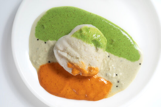 Idli served with tricolor chutney on a white plate