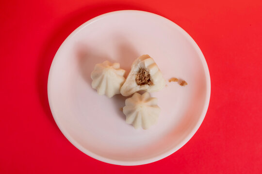Steamed sweet modak rice dumplings on a white plate against a bright red background