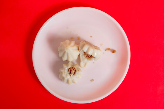 Steamed sweet modak rice dumplings on a white plate against a bright red background