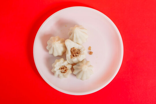 Steamed sweet modak rice dumplings on a white plate against a bright red background