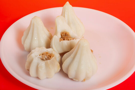 Steamed sweet modak rice dumplings on a white plate against a bright red background