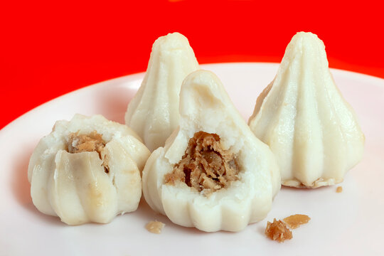 Steamed sweet modak rice dumplings on a white plate against a bright red background