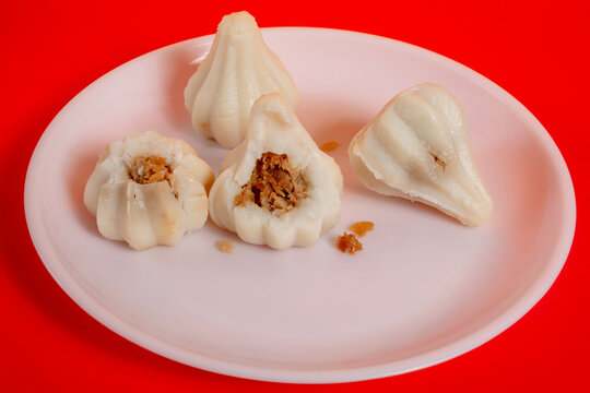 Steamed sweet modak rice dumplings on a white plate against a red background for the Ganesh Chaturthi festival.