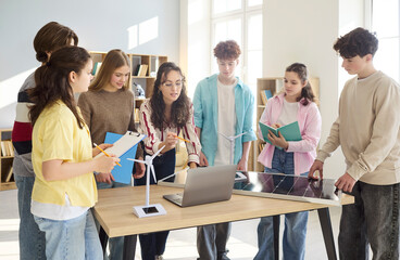 Students and teacher lead classroom energy presentation. During lesson teenagers discuss a model wind turbine and a solar panel, planning projects. Clear concept of renewable energy education. © Studio Romantic