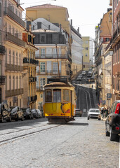 Fototapeta premium Yellow tram traveling up a Lisbon cobblestone street