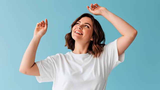 Smiling young woman in white t-shirt dancing with raised arms on blue background