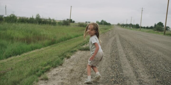 Young boy running down a dirt road with arms outstretched