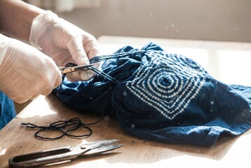 Fototapeta premium Hands in gloves cutting threads on a piece of indigo dyed fabric during traditional shibori crafting process